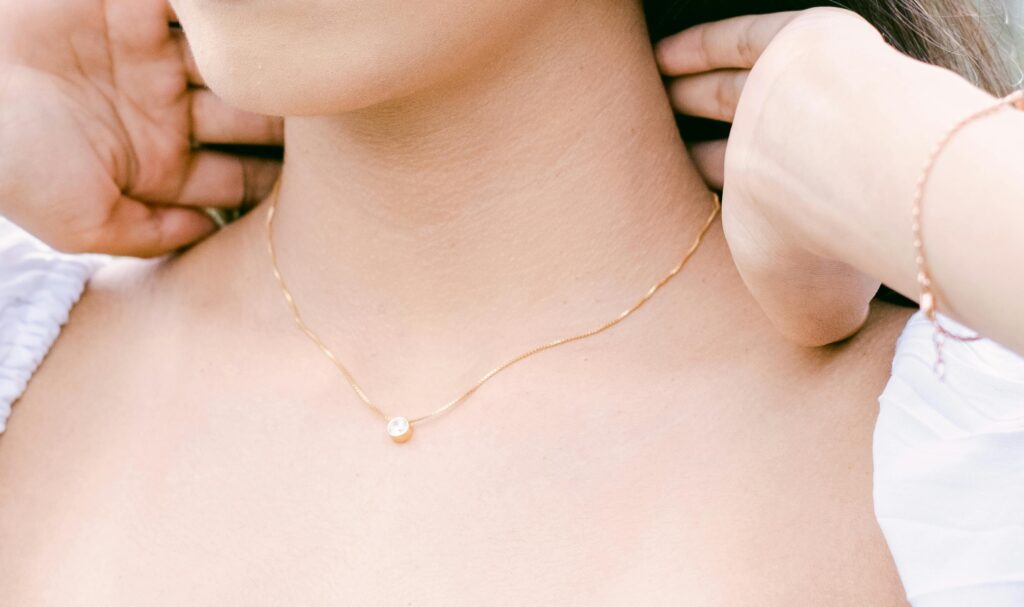 Close-up of a woman adjusting a minimalist gold necklace outdoors in Bali.